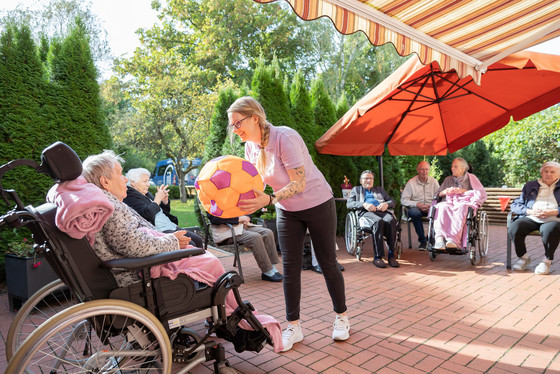 Auf dem Fotos spielt eine Pflegekraft mit Bewohnern Ball auf Terrasse Auf dem Fotos spielt eine Pflegekraft mit Bewohnern Ball auf Terrasse