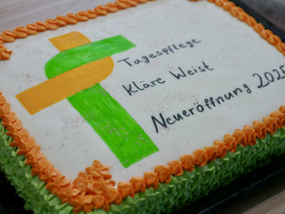 Ein quadratischer Kuchen mit dem grün-orangenen Kreuzband-Logo mit Schriftzug, Zuckerdekor und dem Text "Neueröffnung 2025" bei der Wiedereröffnung der Tagespflegestätte für ältere Menschen im Immanuel Seniorenzentrum Kläre Weist in Petershagen